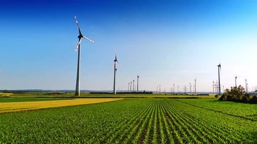 Footage over the green agricultural field. Low angle view at the wind turbines rotating