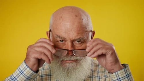 Senior Man Puts On Glasses Against Yellow Background