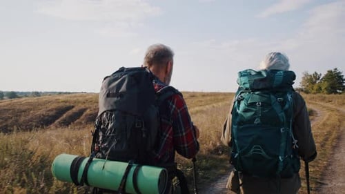 Senior Couple Hiking with Backpacks Through Rural Landscape