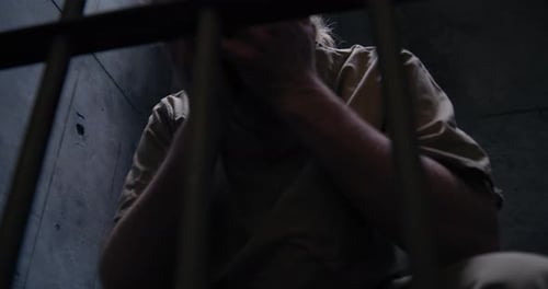 Man in Prison Cell Sits with Face in Hands