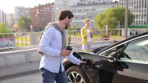 Man Charging Electric Car with Coffee in Hand