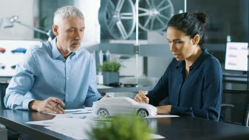 Experienced Automotive Designer and Female Engineer Works with Blueprints and Sketches of a New Car