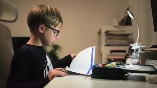 Boy Does Homework At Desk Under Lamp