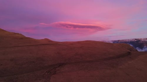 A Magenta Cloud Hovers in the Sky As the Sun Sets Over the Mountain Slope