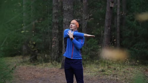 Athletic Man Performing Warmup Exercises and Stretching His Arms and Shoulders Before a Run in a
