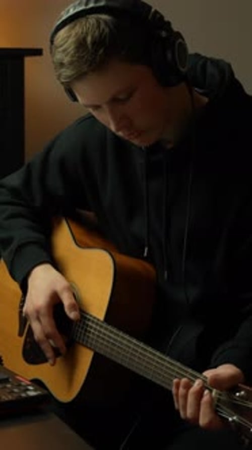 Man Plays Acoustic Guitar Wearing Headphones Indoors
