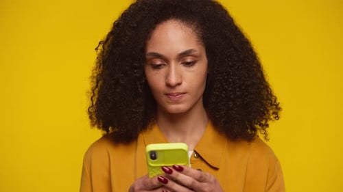 Woman Uses Cell Phone on Yellow Background