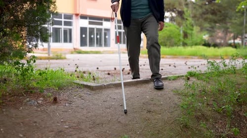 Man with Cane Walking on Urban Sidewalk