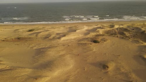 People walking on sand dunes by beach, rotating aerial view