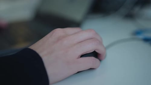 Close-up shot of a hand using a computer mouse at a desk during office work in an indoor business