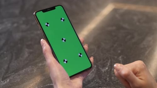 A woman holds a black smartphone in one hand. Green screen, close-up.