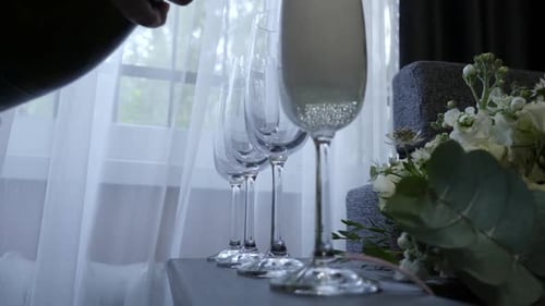 41s. Pouring white, sparkling champagne into glasses. Shot in a dark key.