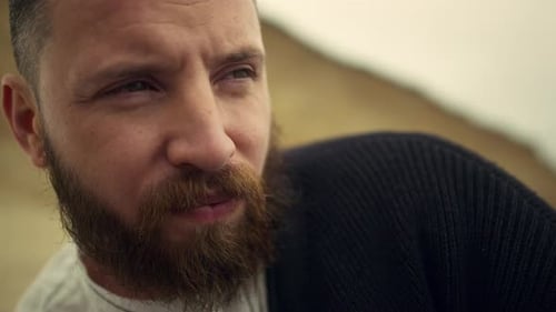 Serious bearded man gazing thoughtfully resting on a beautiful beach at sunset