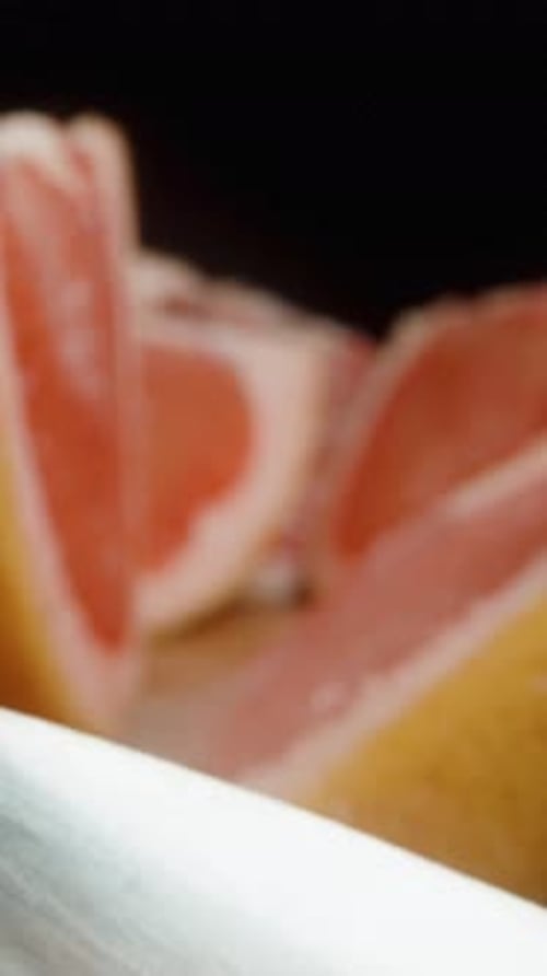Vertical video. Slices of cut grapefruit sprinkled with sugar on a board against a black background.