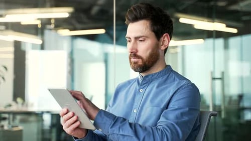 Thoughtful businessman is using digital tablet sitting at workplace in business office. Manager work