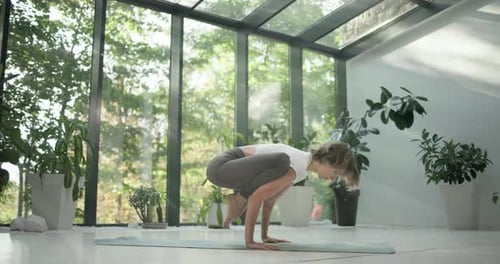 Young Caucasian Fitness Woman Practicing Yoga on a Yoga Mat in a Modern Studio with Plants and Large