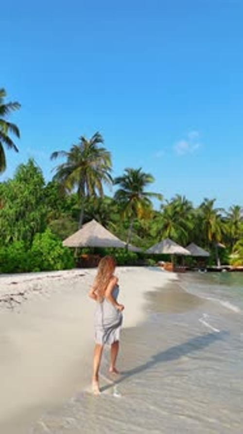 Woman Runs Along the Tropical Beach at Sunset with Long Shadows Cast on the Sand Surrounded By Calm