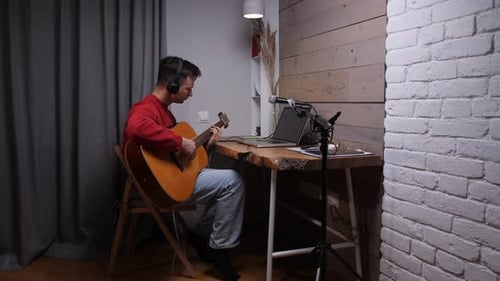 Young Man Plays Guitar at Desk Indoors