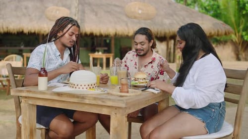 Multiracial LGBTQ Friends Laugh Eat Drink at Tropical Cafe Diverse Group Enjoys Meal Conversation in