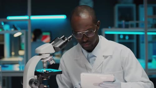 Scientist Using Microscope and Tablet in Laboratory