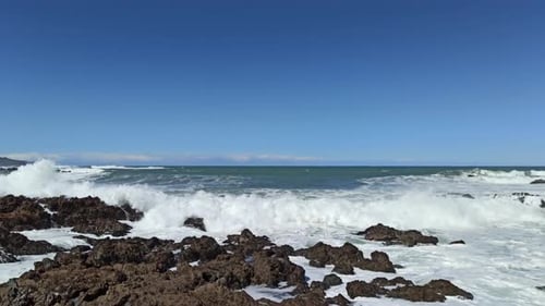 A static shot of rough sea smashing against rocks.