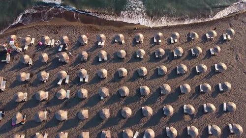 Aerial drone view of sand beach with rows of straw umbrellas and sun loungers by sea with strong wav