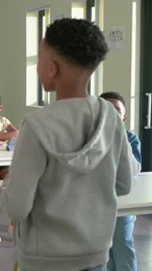 Vertical video: Standing, boy in gray hoodie walking in class, sharing as teacher with tablet
