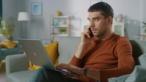 Man on Laptop talking on Phone on Sofa