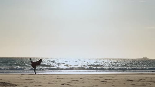 Graceful Young Woman in a Long Red Dress Dancing Alone on the Beach at Early Sunset