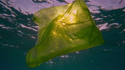 bolsa de plástico amarilla desechable que se desplaza lentamente por debajo de la superficie del agua bajo los rayos del sol al atardecer