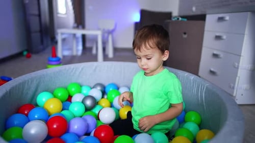 Sweet toddler sitting in the dry pool with an orange ball in his hands.