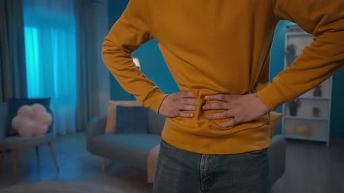 A Man is in Pain While Standing in the Living Room Hands of a Man Holding Kneading His Stomach Close