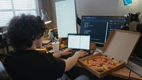 Man Coding Software on Laptop with Pizza on Desk at Home
