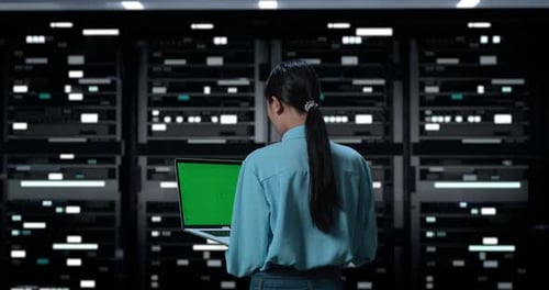Back View Of A Woman Working On Green Screen Laptop In Server Room Database