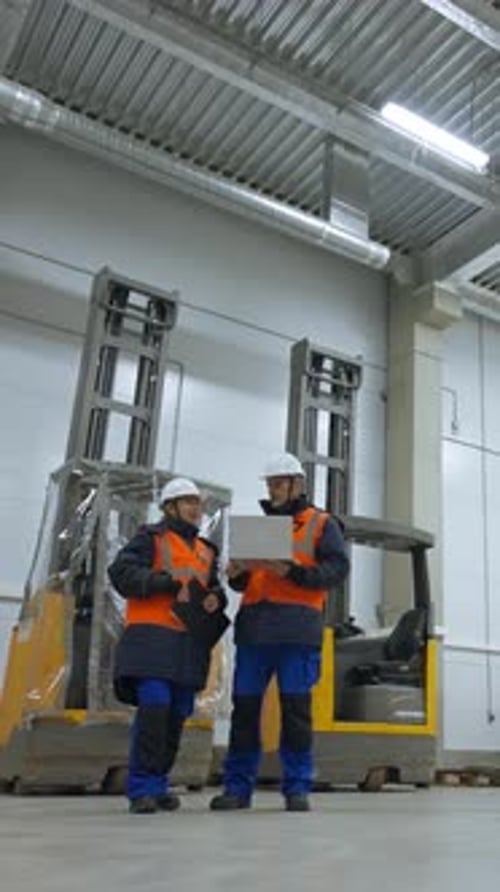 Vertical of Engineers Stand in Terminal of Warehouse Looking in Laptop