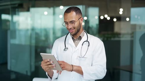 Portrait of a young smiling doctor using a tablet while standing in a clinic. Handsome mixed race