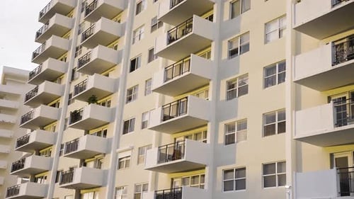 Gelbes Mehrfamilienhaus mit Balkonen bei Tageslicht an einem sonnigen Tag mit vorbeifliegenden Vögel