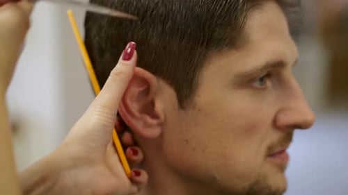 Adult caucasian male having haircut in salon, closeup of scissors cutting hair
