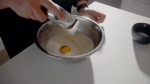 Young Female pouring sugar in a bowl with milk and eggs making dough for a cake in the kitchen at ho