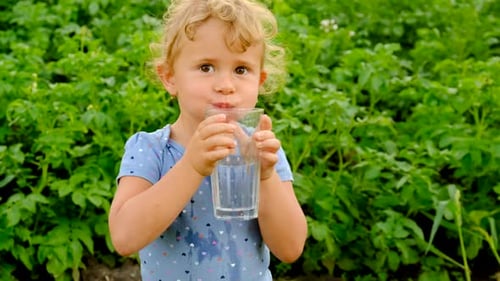 a Child Drinks Water in the Garden Selective Focus