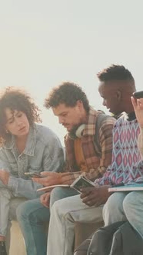 Students sit next to the university looking at their mobile phones and talking