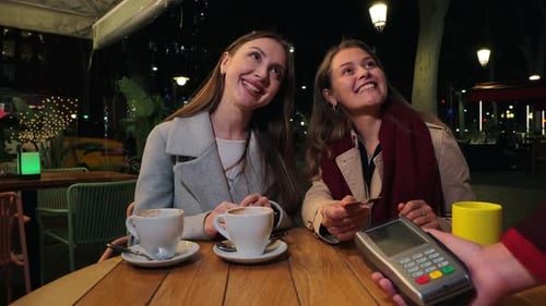 Two Women Paying at an Outdoor Cafe at Night