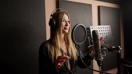 girl singer singing in a recording studio with headphones in front of microphone to create a song