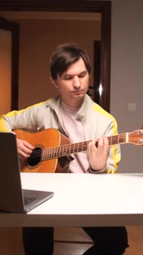 Man Plays Acoustic Guitar Indoors at Table