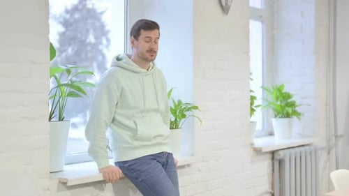 Man Leans Against Window Sill and Thinks