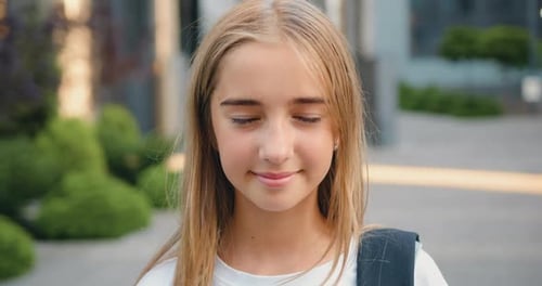 Close up portrait of smiling female elementary school student wearing backpack standing outside