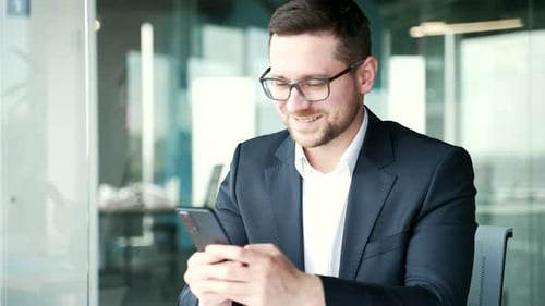 Businessman in formal suit is using smartphone at workplace in business office. Worker reads