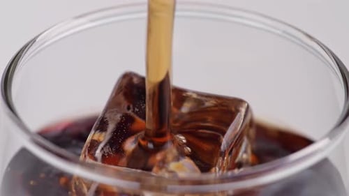 Close Up Of Fresh Cola Being Poured In To The Glass With Ice Cubes On White Background