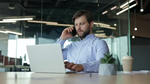 Man Working on Laptop and Talking on Phone