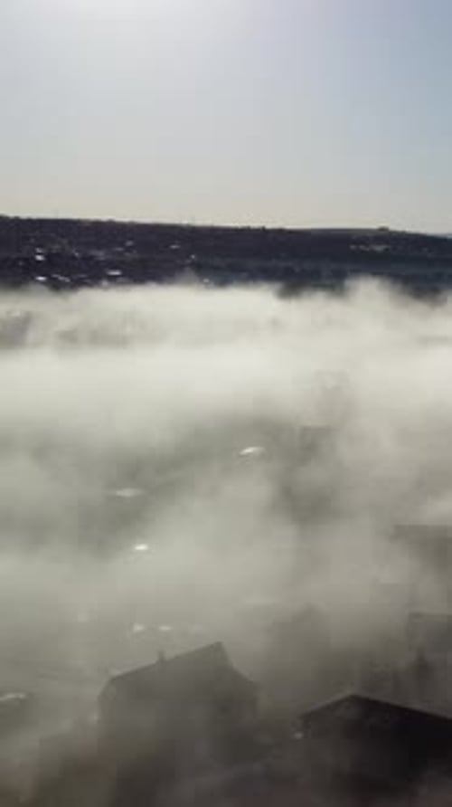 Aerial Vertical View Blue Sky Sun and Fog Over Residential Houses Near Sea The Drone Flies Over